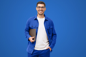 Young smiling modern man or male teacher holding laptop, isolated on blue