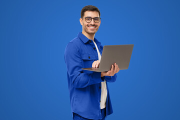 Portrait of modern businessman standing holding laptop and looking at camera with happy smile