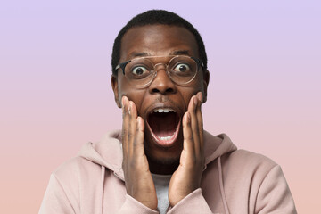 African guy on purple background, wearing round spectacles, looking extremely surprised