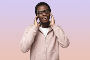 Happy black man in pink hoodie, holding earphones with hands, listening to music wiht closed eyes