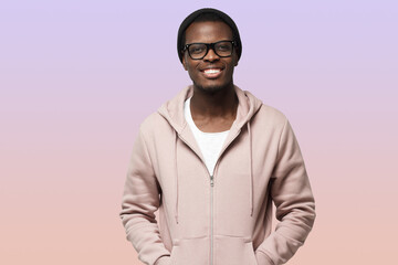 Obraz premium Portrait of smiling handsome african american guy in pink hoodie standing isolated on purple