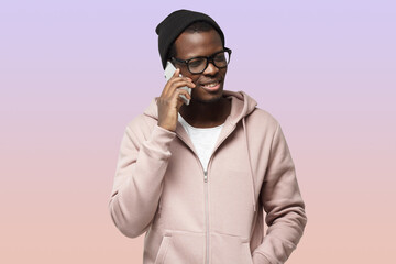 African American male on purple background in hipster clothes and big glasses, talking on phone