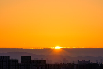 Fototapeta na wymiar 都市の夜明け。日の出とともに空と雲がオレンジ色に染まり、ビル群はシルエットとして写す
