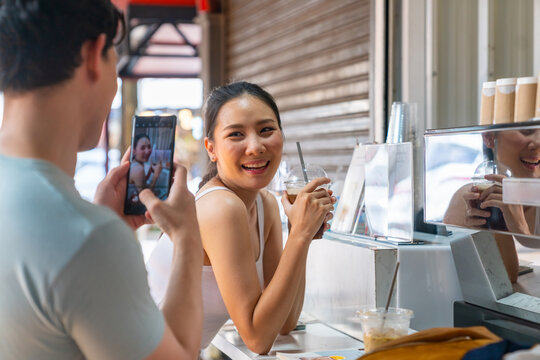 Asian couple enjoy and fun outdoor lifestyle shopping at street market on summer holiday vacation. Handsome man using mobile phone photography his girlfriend while shopping together at weekend market