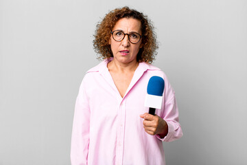 pretty middle age woman feeling puzzled and confused. tv presenter with a microphone concept