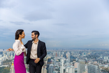 Caucasian couple celebrating holiday event having dinner at luxury skyscraper outdoor rooftop restaurant bar at summer sunset. Man and woman enjoy city lifestyle looking at city skyline in the evening