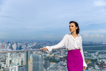 Portrait of Confident Caucasian executive businesswoman standing at skyscraper office building outdoor rooftop looking to city skyline and office building in metropolis at summer sunset.