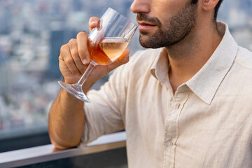 Fototapeta premium Portrait of Confident Caucasian man enjoy outdoor lifestyle drinking wine while celebrating holiday dinner party at skyscraper rooftop restaurant and bar with looking to city skyline at summer sunset.