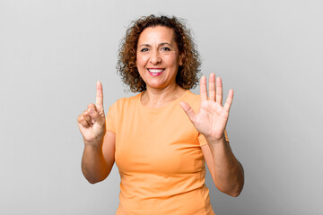 middle age hispanic woman smiling and looking friendly, showing number six or sixth with hand...