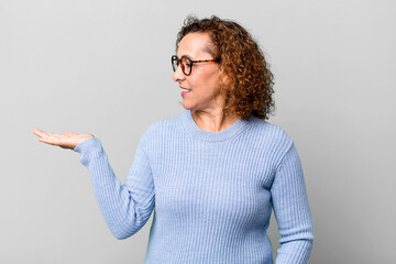middle age hispanic woman feeling happy and smiling casually, looking to an object or concept held...