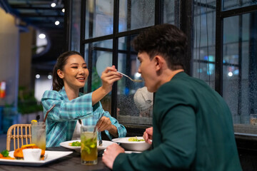 Asian couple celebrating holiday event at luxury restaurant bar in the city at night. Attractive man and woman enjoy city lifestyle shopping and having dinner with food and drink on travel vacation