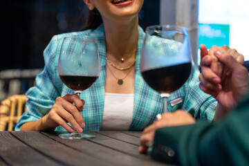Happy Asian couple celebrating holiday event at luxury restaurant in the city at night. Man and woman enjoy city lifestyle having dinner and drinking wine together at bar terrace on travel vacation