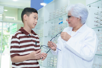 Middle-aged ophthalmologist examining young boy and giving eye consultation to Asian boy