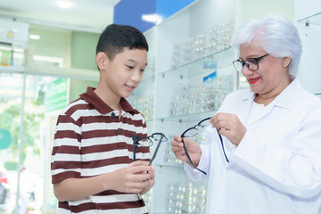 Obraz premium Middle-aged ophthalmologist examining young boy and giving eye consultation to Asian boy