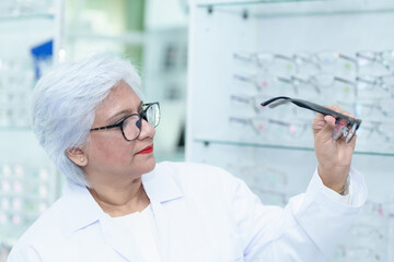  Middle aged ophthalmologist holding eyeglasses and examining them, focus on eyeglasses, close-up