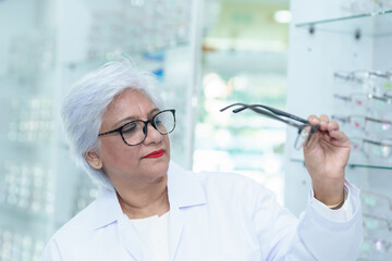  Middle aged ophthalmologist holding eyeglasses and examining them, focus on eyeglasses, close-up