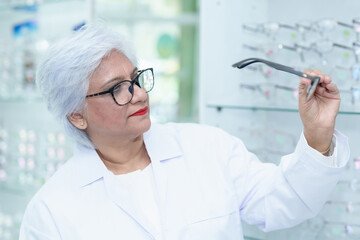  Middle aged ophthalmologist holding eyeglasses and examining them, focus on eyeglasses, close-up