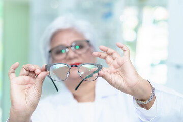  Middle aged ophthalmologist holding eyeglasses and examining them, focus on eyeglasses, close-up