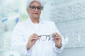  Middle aged ophthalmologist holding eyeglasses and examining them, focus on eyeglasses, close-up