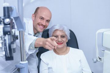 Attractive male ophthalmologist is checking eye vision of middle aged woman in modern clinic,...