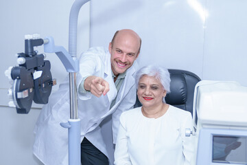 Attractive male ophthalmologist is checking eye vision of middle aged woman in modern clinic,...