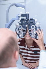 Asian boy looking through optical phoropter during eye exam, diagnostic ophthalmology equipment, selective focus