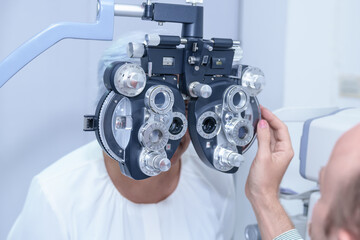 Senior Asian woman looking through optical phoropter during eye exam, diagnostic ophthalmology equipment, selective focus