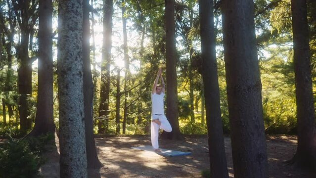 Caucasian adult man holds tree pose  vrikhasana in yoga session in pine tree forest.