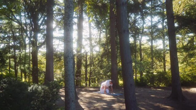 Close up shot caucasian adult man dressed in white doing yoga in a pine tree forest.