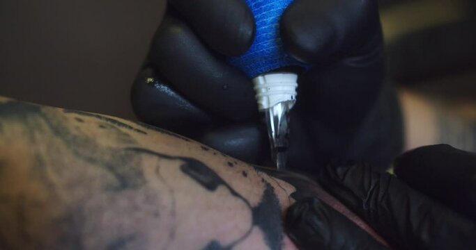 Amazing detail shot of a professional tattoo artist's ink machine during the process of tattooing a man's arm.