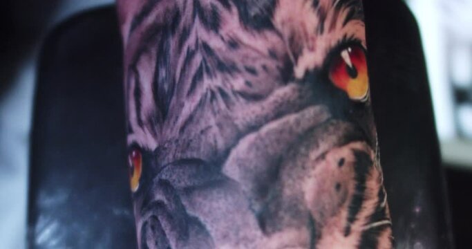 Close-up detail of the orange eyes of a tiger tattoo on the forearm of a man