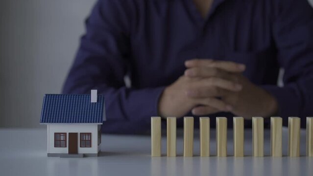 Hand stops the wooden domino from falling onto the model house. hedging and insurance concepts