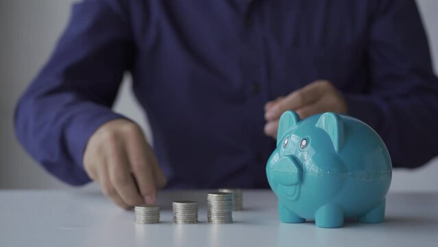 Young man putting coins in a piggy bank, saving money concept. 4k