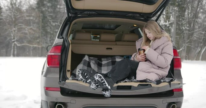 Teenage girl with thermos sitting in car trunk