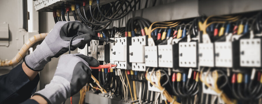 Electricity and electrical maintenance service, Engineer hand holding AC multimeter checking electric current voltage at circuit breaker terminal and cable wiring main power distribution board.