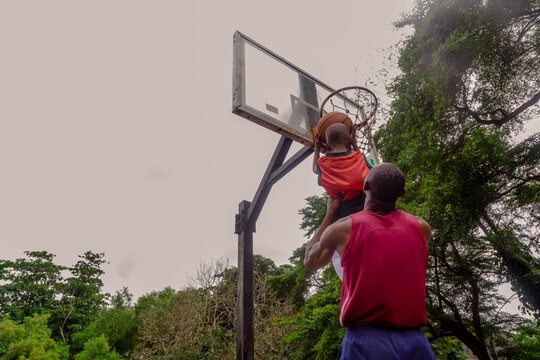Father lifting son up to make a basket at basketball court