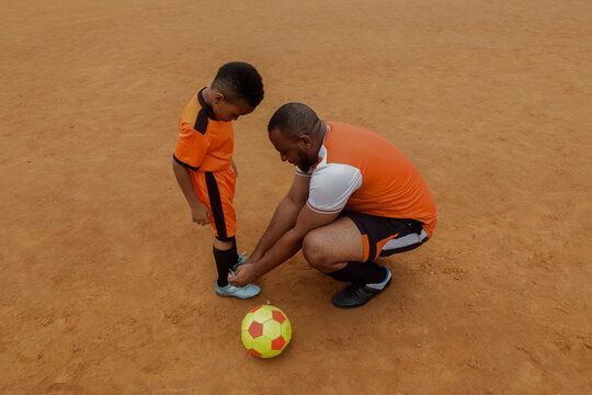 Father ties shoe lace for little son on field
