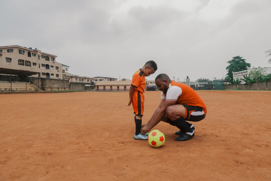 Father helping son tie shoelace on soccer field