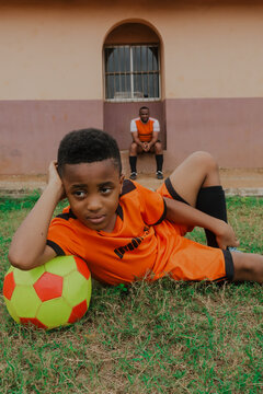Son resting on soccer ball while father observes in background