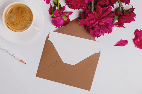 Greeting card in the envelope, flat lay with coffee and pink peonies, mockup