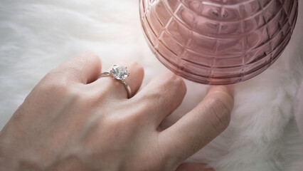 Close up of an elegant diamond ring on woman finger with white feather background. love and wedding...