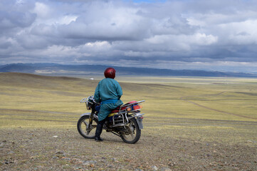 Fototapeta na wymiar Mongolian on a motorcycle on a hill looks at the steppe