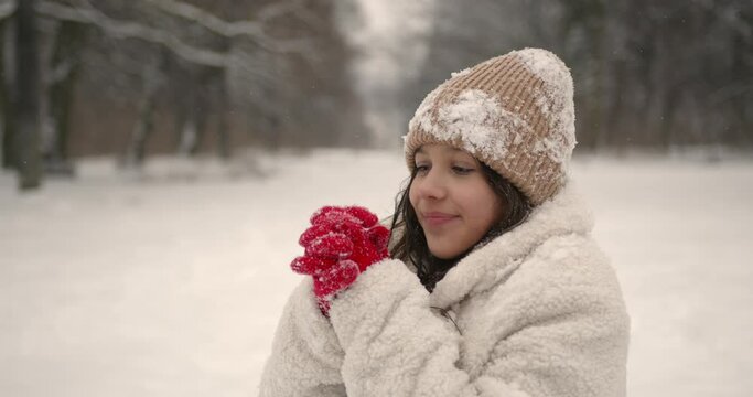 Beautiful girl in snowflakes getting warm in winter forest