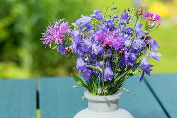 Naklejka na ściany i meble Fresh beautiful summer bouquet of blue field bells with cornflowers in a vase on a garden table.