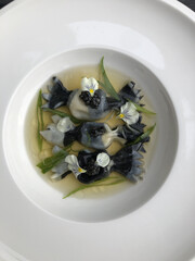 Squid ink gyozas in the shape of caramelle pasta with awase dashi, caviar, scallions, and orange-infused oil
