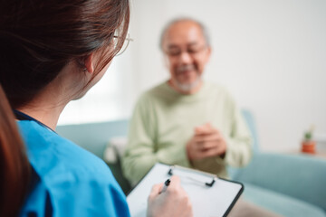 Obraz premium Asian caregiver talking senior male patient checkup in living room at home. Older elderly man consults after physical therapy. Nurse assistance rescue concept.