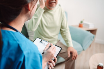 Asian caregiver talking senior male patient checkup in living room at home. Older elderly man consults after physical therapy. Nurse assistance rescue concept.