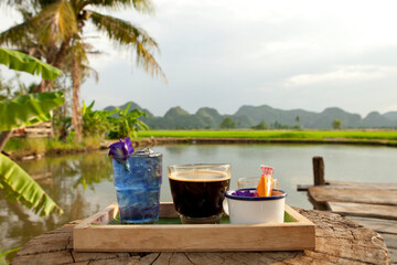 Coffee and Butterfly Pea Tea on the rice fields background. Beautiful Nature in Kanchanaburi, Thailand. Coffee with a View.