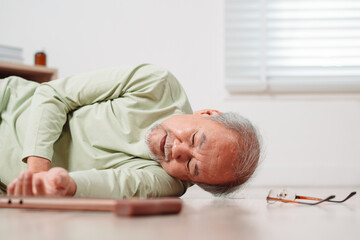 Fototapeta premium Asian senior man falling on the ground with walker in living room at home. Elderly older mature male having an accident heart attack for emergency help support from hospital. Insurance health care.