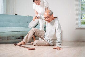 Asian woman daughter or granddaughter helping senior male from falling on the ground in living room at home. Elderly old mature grandfather having an accident heart attack after doing physical therapy